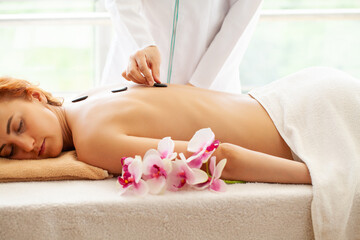 Obraz na płótnie Canvas Young woman getting hot stone massage in spa salon.