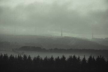 hügelige Berglandschaft im Nebel mit riesigen Windrädern, mystische Stimmung 