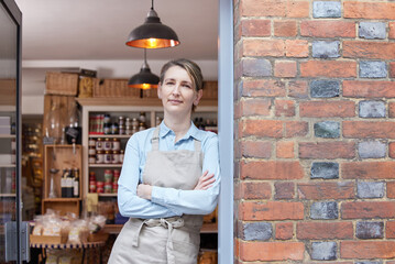 Portrait Of Female Owner Standing In Doorway Of Delicatessen  Food Shop