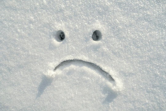 Sad smiley face drawn in the snow on a sunny winter day. Copy space. Negative emotions. 