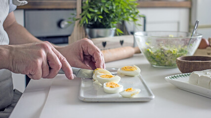 Male chef cuts boiled eggs with a knife on a board close-up