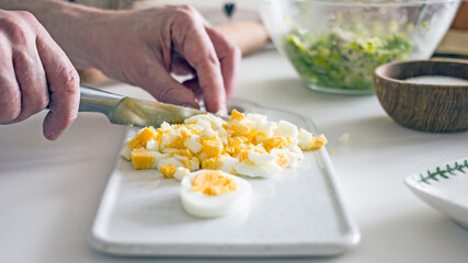 Male chef cuts boiled eggs with a knife on a board close-up