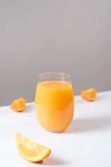 Jugo de naranja en un vaso de cristal con trozos de naranja sobre una mesa blanca con un fondo gris