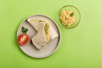 Vegan pita bread roll with hummus and salad on a green background.