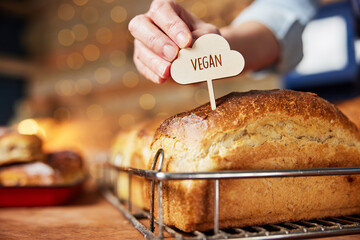 Sales Assistant In Bakery Putting Vegan Label Into Freshly Baked Baked Sourdough Loaves Of Bread