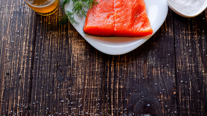 A piece of lightly salted salmon, salt and olive oil on a dark table