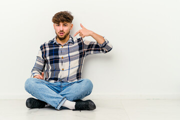 Young Moroccan man sitting on the floor isolated on white background person pointing by hand to a shirt copy space, proud and confident