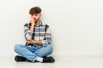 Fototapeta premium Young Moroccan man sitting on the floor isolated on white background biting fingernails, nervous and very anxious.