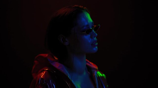 Slow motion girl moving in neon light on black background. Beautiful girl dancing in lights wearing sunglasses. Art design of female disco dancing, Night club, Party. FHD footage. 