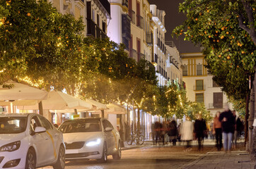 Blurry people walk along busy illuminated street of Sevilla. Spain