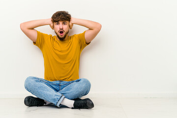 Young Moroccan man sitting on the floor isolated on white background screaming with rage.