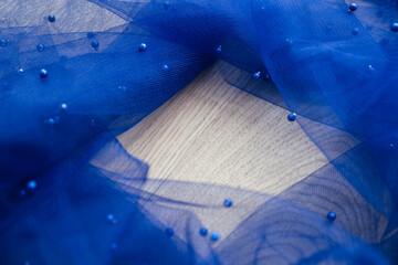 Close up picture of dark blue tulle fabric with pearls laying on the wooden background. Crumpled tulle with small beads. Abstract wallpaper for the fashion industry with copy space for text.