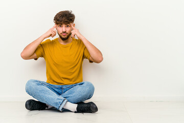 Young Moroccan man sitting on the floor isolated on white background focused on a task, keeping forefingers pointing head.