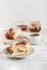 A sweet, freshly baked bun with jam on a white wooden board is cut into pieces.