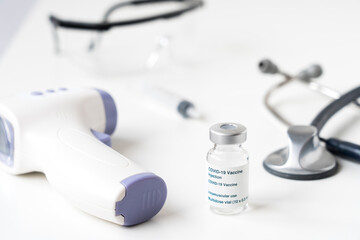 Close-up of a coronavirus vaccine next to a digital thermometer and medical accessories on a white...