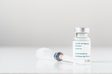From view of a glass vial with Covid vaccine next to a syringe on a white background. Copy space