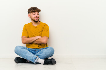 Young Moroccan man sitting on the floor isolated on white background laughing and having fun.