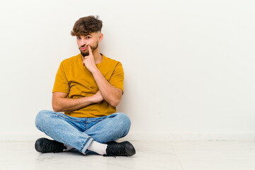 Young Moroccan man sitting on the floor isolated on white background unhappy looking in camera with sarcastic expression.