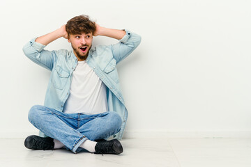 Young Moroccan man sitting on the floor isolated on white background screaming, very excited, passionate, satisfied with something.