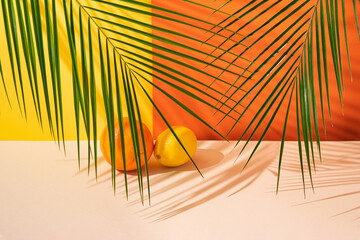 A fresh orange and a juicy lemon placed in a green palm leaf shade in front of vibrant yellow and...