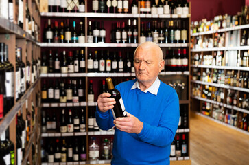 Attentive pensioner chooses red wine in a liquor store. High quality photo