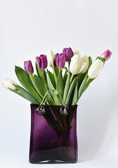 Bouquet of white and lilac tulips in a glass purple vase in the form of a handbag on a white background.