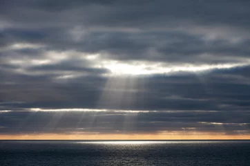 Fotobehang The sun bursts through dark storm clouds over the sea in Cornwall © Simon
