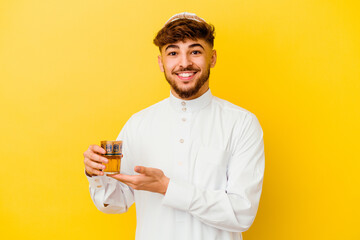 Young Moroccan man wearing the typical arabic costume drinking tea isolated on yellow background