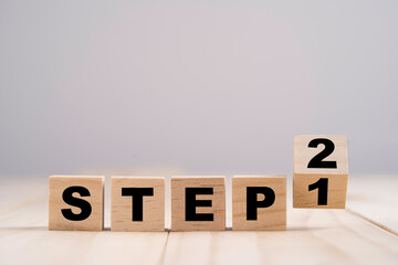 Flipping wooden cubes block for changing step 1 to step 2 on wooden table.