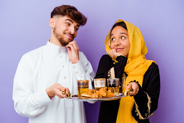 Young Moroccan couple drinking tea celebrating ramadan month isolated on purple background