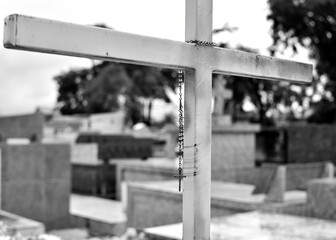 Black and white. A crucifix hanging from a cross in a cemetery in a cloudy day. Shallow depth of field.