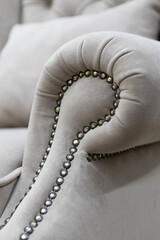 Armrest of a soft chair in a gray velvet fabric with decor made of decorative nails without people close-up