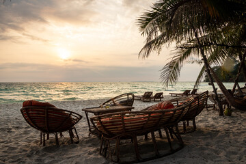 wood chairs and hammock on a background of a beautiful small island and wight beaches on big ocean with trees and palms of coconut and a part of a local port and bungalow wood before the sunset