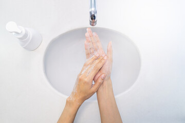 Fototapeta premium Close up of woman washing her hands for protection, and soap pressed bottle sinks top view.