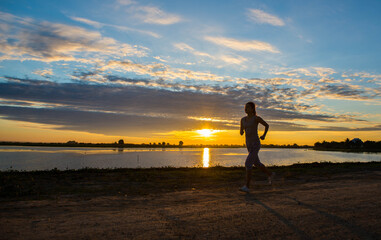 Obraz premium A Beautiful woman jogging in the morning above the dam at the sky sunset.