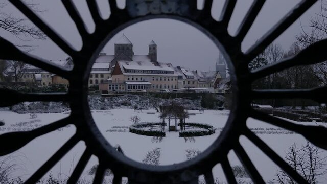 Slow forward tracking through the center of an old iron gate with fresh snow in the public gardens with a cityscape of churches and spires in the German city of Hildesheim.