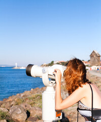 Young woman looking through binocular viewer on the sea landscape. Bulgaria. Nesebar. Black Sea coast.