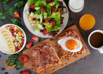 variety of open sandwiches made of brown whole wheat  bread with tomatoes sauce, bowl of oat granola with yogurt, white beans, bacon, fried egg. fresh fruit and vegetable salad, healthy breakfast.