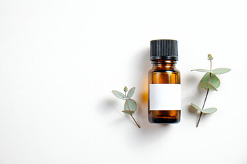 Brown transparent glass bottle with black cap and blank label with copy space for text or logo, white wood textured table background. Essential oils for aroma therapy. Close up, copy space, top view.