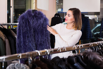 Obraz na płótnie Canvas Charming female customer examining blue fur coats in women cloths store