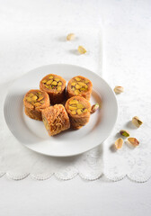 Baklava rolls with pistachio nuts served on a white plate. Traditional Arabic or Mediterranean authentic dessert.