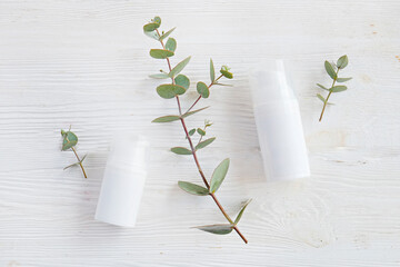 Two plastic bottles of different size with the dispenser cap and blank label with copy space for text or logo, white wood textured table background. Eucalyptus leaves as decor. Close up, top view.