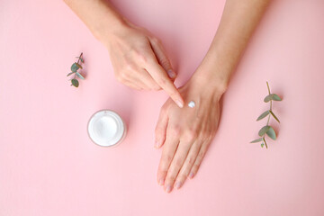 Young woman performing everyday skincare routine, applying moisturizing lotion. Revitalizing hand cream for healing and recovery from dryness. Copy space, close up, pink background, flat lay, top view