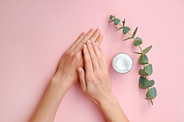 Young woman performing everyday skincare routine, applying moisturizing lotion. Revitalizing hand cream for healing and recovery from dryness. Copy space, close up, pink background, flat lay, top view