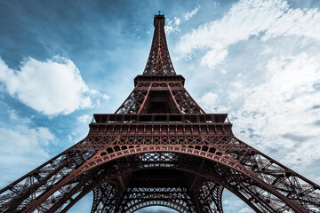 Ultra wide angle of Eiffel Tower over blue sky with white clouds and bright glow of sun in Paris, France. Worms eye view of the entire monument with all little details. Scene with high dynamic range.