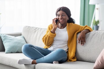 Obraz premium Beautiful african american woman sitting on couch, talking on phone