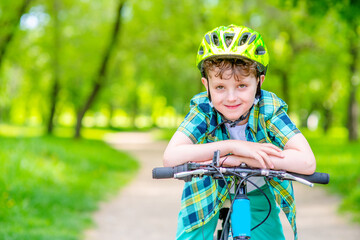 A boy with a green bicycle helmet on his head rides his bicycle in the summer park. Summer rest