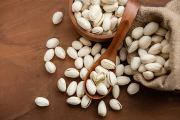 Pistachios in a wooden spoon. Wooden bowl with nut pistachios. on a wooden background, near a bag from burlap. Healthy food and snack, organic vegetarian food. (selective focus; close-up shot)