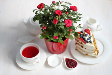 Holiday still life with Red roses flowers on white table with tea crockery set and cream cake with strawberries and blackberries