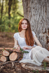 Red-haired peasant girl sitting on the ground in the forest. Red-haired peasant girl in the forest...